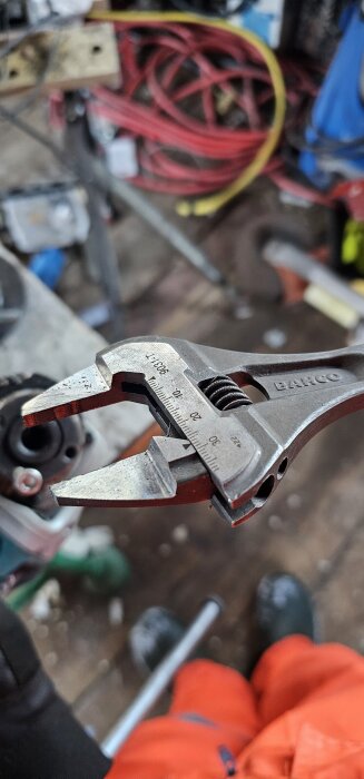 En Bahco 9031-T skiftnyckel visas, med fokus på käftarna, omgiven av verktyg och kablar i en verkstadsmiljö.