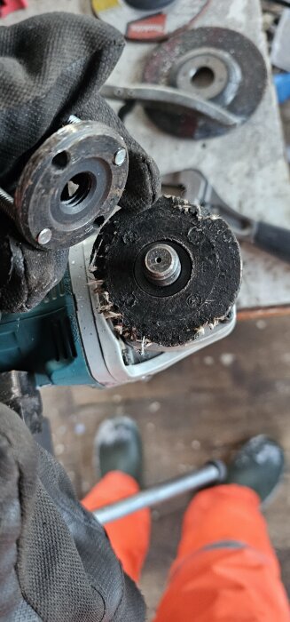 Nära bild på en trasig vinkelslip med borttagen skiva och låsmutter, hållna av en handske på en verktygsbänk.