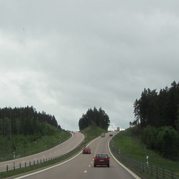 En väg som delar sig över en kulle med bilar körande under en mulen himmel.
