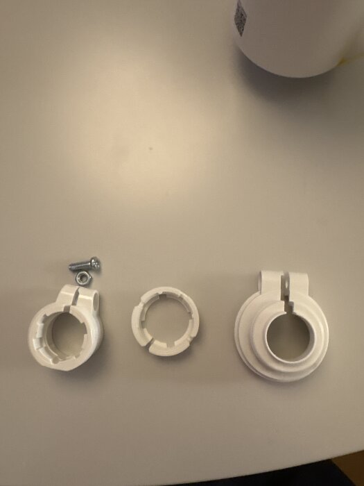Vita termostatadaptrar och skruv på ett bord, olika storlekar för elementanslutning.