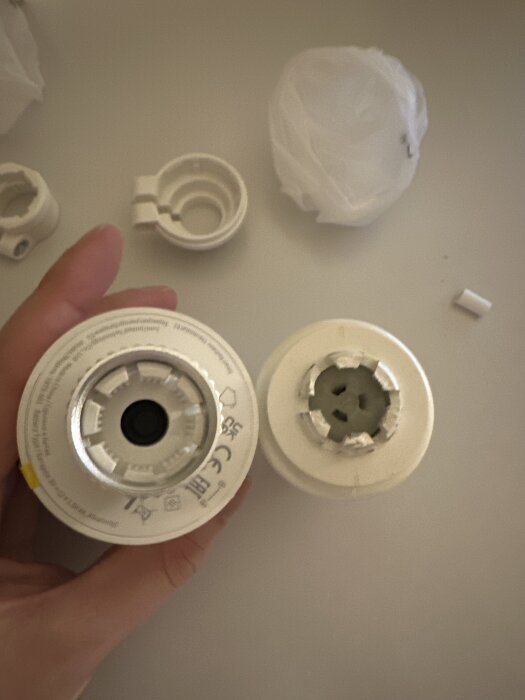 Närbild av två termostatadaptrar i olika storlekar och former, med ytterligare delar och en hand synlig i bakgrunden.