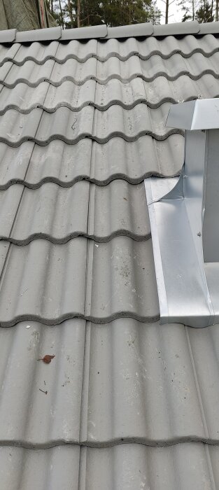 Grå takpannor med en glipa nära en metall huv. Dalgången ser försvagad ut.