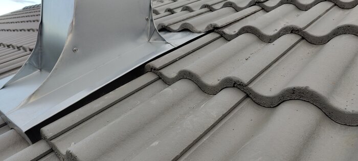 Närbild på tak med plåttakhuv och betongpannor som har glipor och ojämn placering där takhuven möter taket.