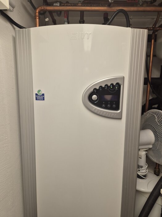 IVT värmepump i vit färg med kontrollpanel och kopparrör ovanpå i ett tekniskt rum.