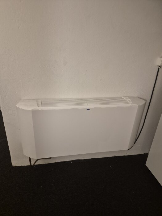 Bild av en vit väggmonterad radiator eller element, placerad i ett rum med mörk matta.