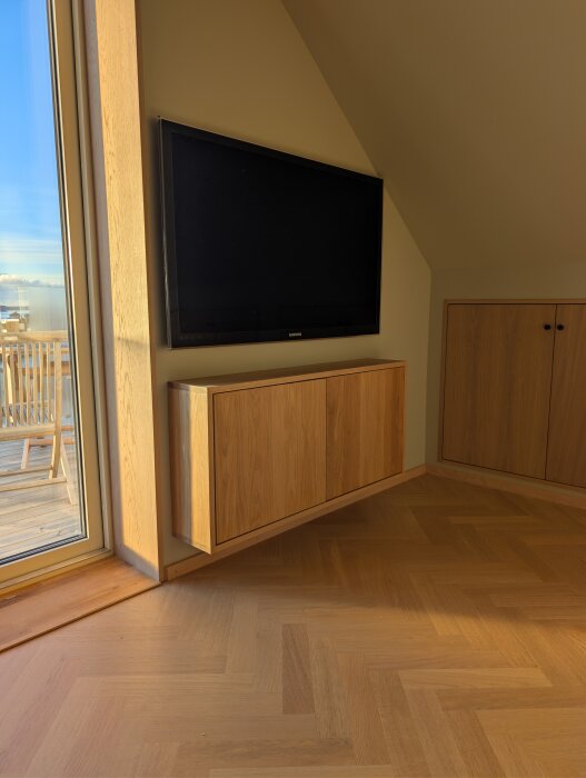 Väggmonterad tv-bänk av massiv ek under en stor platt-tv i ett sovrum.