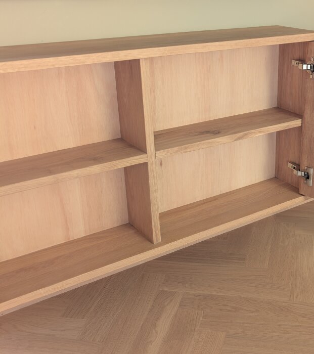 Handbyggd tv-bänk i massiv ek med öppna hyllor och en dörr, monterad på en parkettgolv.