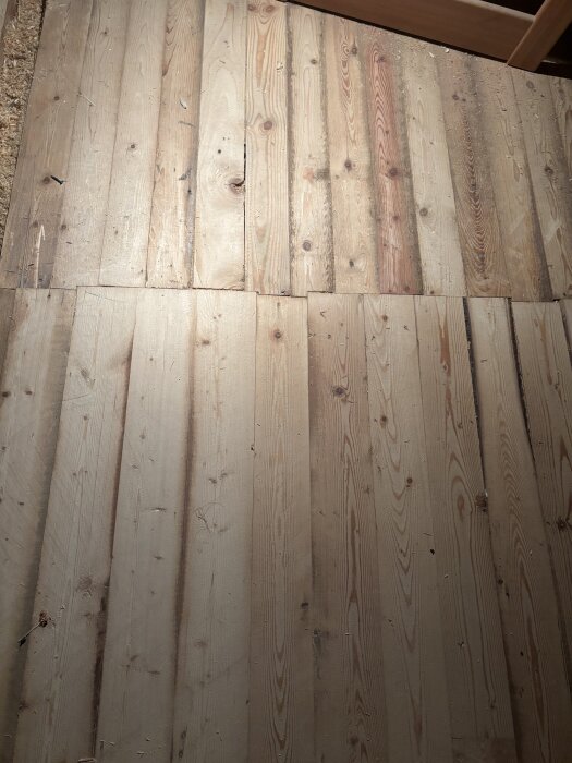 Äldre trägolv med slitna plankor, kvistutslag och generella ojämnheter i ett gammalt hus från tidigt 1900-tal.