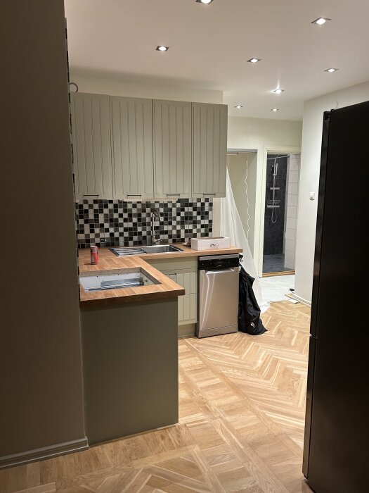 Kök med svartvit kakel, bänkskiva i trä och en fristående diskmaskin placerad vid diskhon.