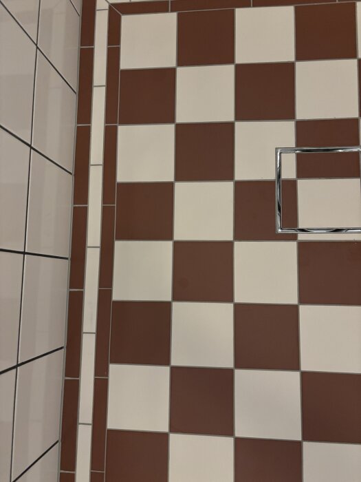 Närbild av ett rutigt golve i badrum med röda och vita plattor. Vatten ligger kvar på ett fåtal plattor nära en vägg.