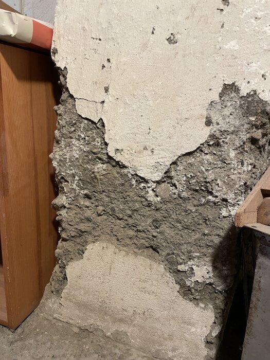 En gammal källarvägg med flagnande puts och synlig ojämn betong, delvis trasig och i behov av reparation.