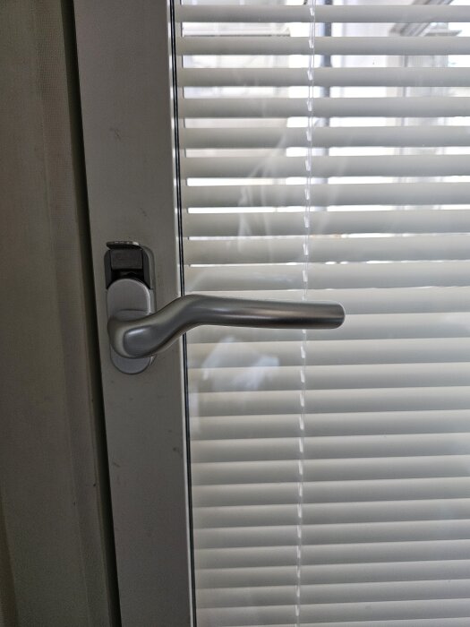 Balkongdörr med låst handtag, vit persienn i bakgrunden.