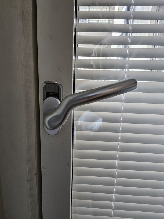 Balkongdörr med låshandtag i låst läge bredvid jalusi.