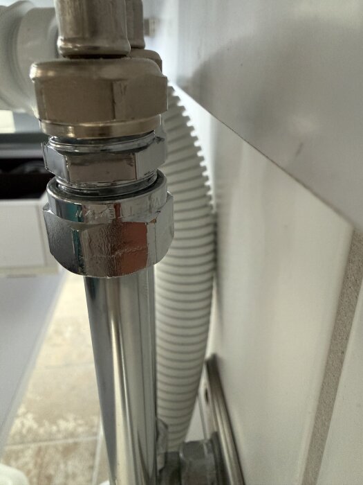 En närbild av en metallisk Vatette-koppling installerad under ett handfat med anslutna rör och slangar.