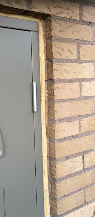 Talon oviaukko, jossa näkyy eristetty ovireuna, harmaa ovi ja ruskeat tiilet.