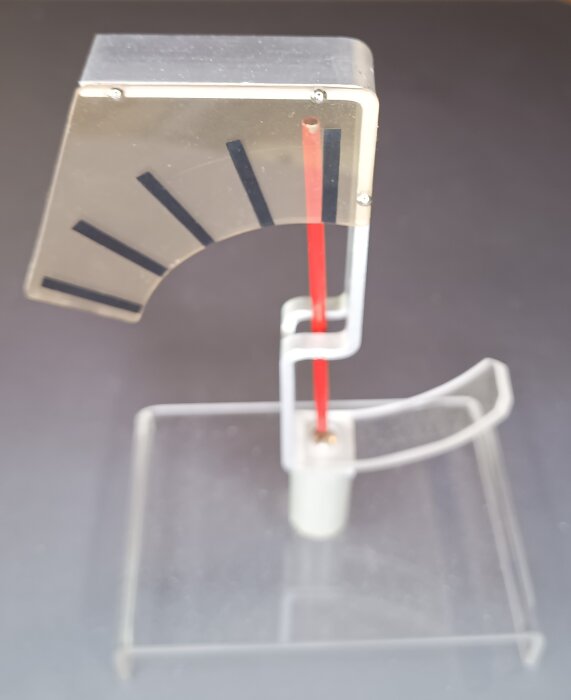 Enkel elektroskopmodell med röd stång och genomskinlig bas, redo att användas med kattskinn och ebonitstav.