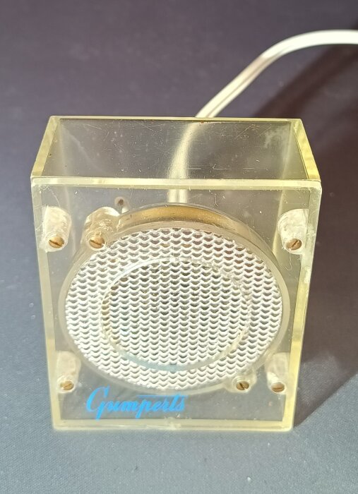 Kolkornsmikrofon i genomskinligt hölje med metallgaller synlig, kopplad med vit sladd.