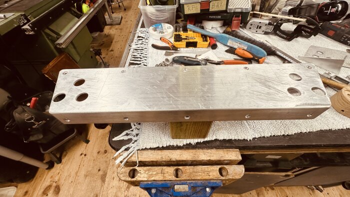L-formad aluminiumprofil med borrade hål ligger på en arbetsbänk omgiven av verktyg, används för att förstärka en trampbåts räcken.
