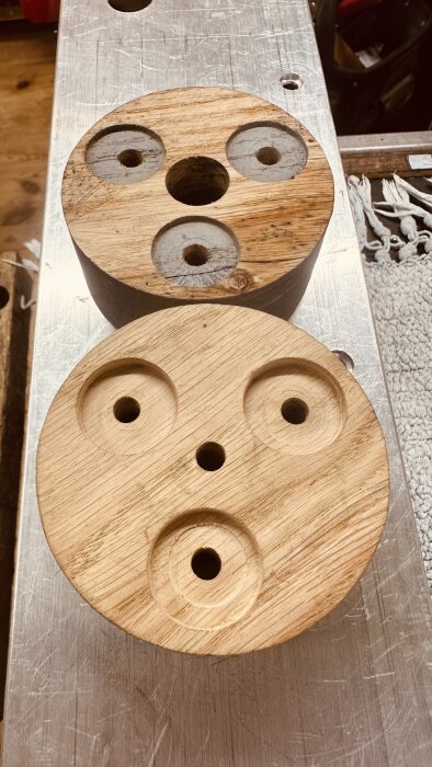 Två runda träskivor med hål, placerade på ett metallbord i en snickarmiljö.