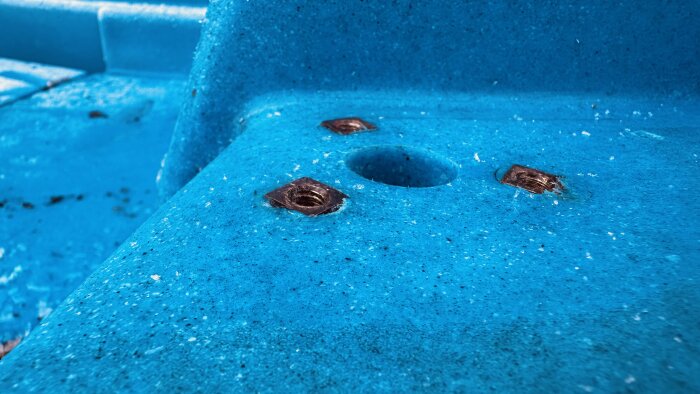 Blå plastyta på en båt med synliga inbäddade metalldelar och hål för montering av rostfria räcken.