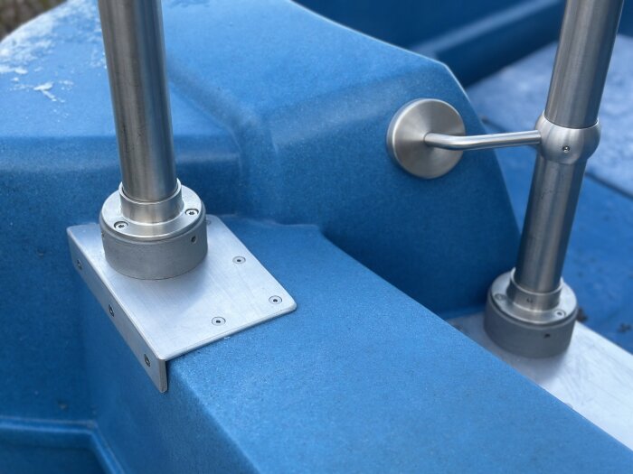 Stålräcken monterade på en blå trampbåt, med aluminiumfäste och skruvdetaljer synliga.