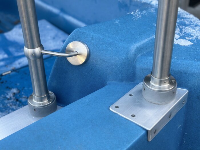 Rostfritt stålräcke monterat på blå plastbåt med förstärkning i aluminium, synliga skruvar och ledstängsfästen.