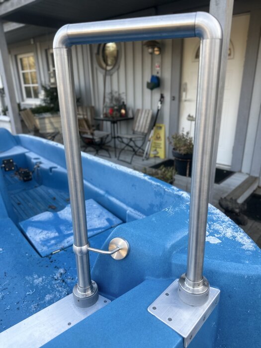 Nya rostfria räcken monterade på en blå trampbåt, med tydliga metallfästen och en utomhusbakgrund av altan och utemöbler.