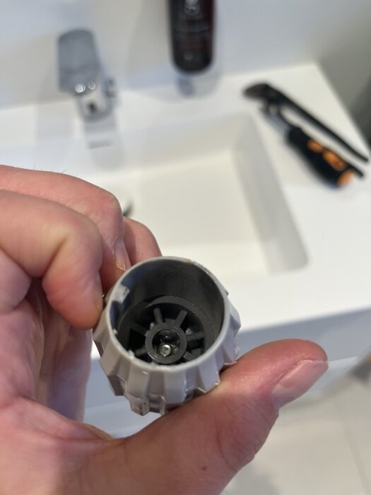 Termostat-vred i närbild hålls i en hand över ett handfat. I bakgrunden syns verktyg på en vit yta.