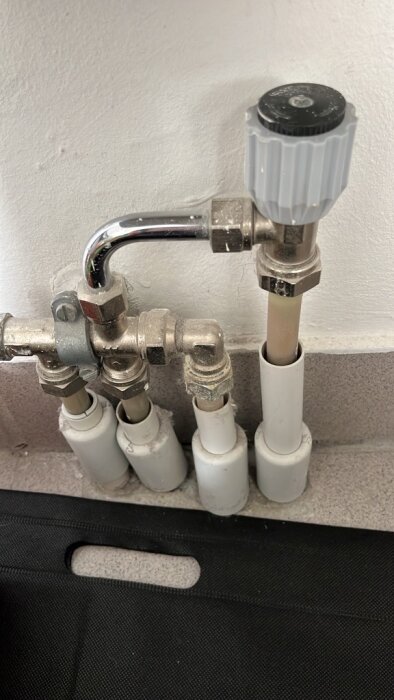 Golvtermostater med rör och ventil på en vit vägg, antagligen från en byggnad uppförd 1989, som behöver uppdateras.