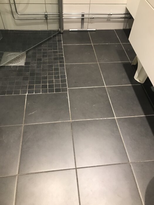 Klinkergolv med slitna och missfärgade fogar i ett badrum, särskilt i duschhörnan, med fokus på önskemål om renovering och underhåll.