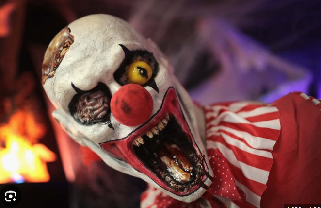 Skrämmande clownmask med röd näsa och blottade tänder i ett halvmörkt rum med dämpad belysning.