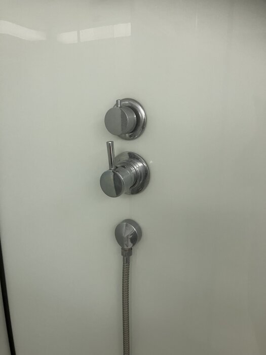 Engreppsblandare i duschkabin med två handtag och ansluten duschslang, övre för flöde och nedre för temperatur.