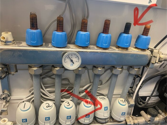 Styrdonet till golvvärme visas löst monterat, med termometrar och vred markerade med siffror och pilar pekande på vissa komponenter.