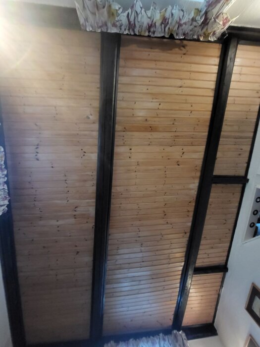 Tak med mörka ekbjälkar och furupanel i ett gammalt hus, potentiellt målade med mörk färg.