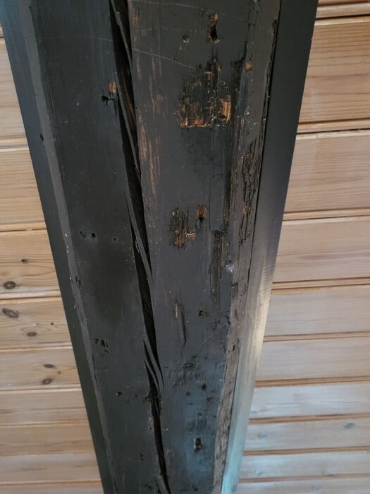 Gammal mörk målad bjälke och trätakspanel i ett hus från tidigt 1900-tal. Bjälken har slitage och ligger mot ljusare träpanel.