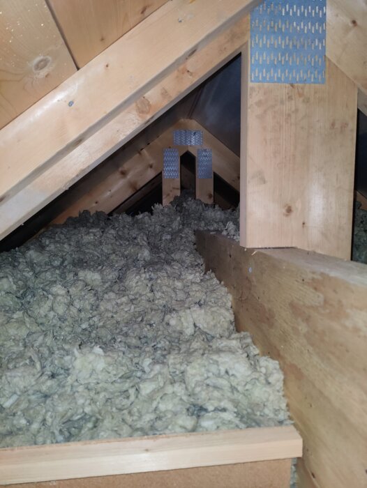 Vind med träbalkar och isolering. Svartmögel syns på balken nära vinden där fuktkvot mättes. Takstolarna är fria från mögel.