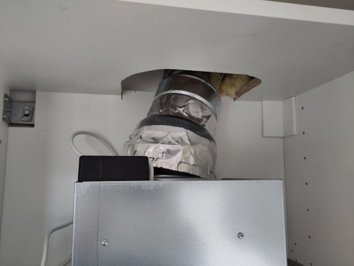 Ventilationsrör installerat i ett 40 cm skåp med en fläkt, sett underifrån med silvertejp och isolering synlig i taket.