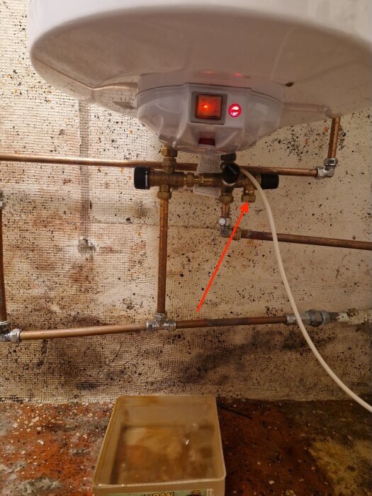 Varmvattenberedare med kopparrör och säkerhetsventil över en golvbrunn.