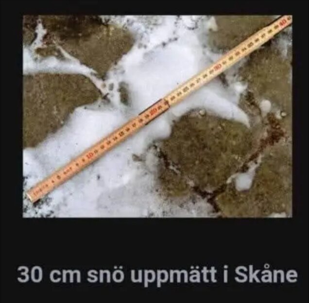 Måttstock visar 30 cm snö på mark med gräsmatta i Skåne.