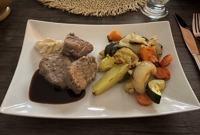 Fläskfilé med rödvinssås, pepparsås och ugnsstekta grönsaker på tallrik.
