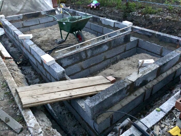 Grunden för en byggnad med murade lecablock på betongsula, med en skottkärra och vattenpass i mitten.