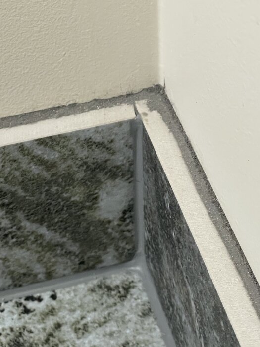 Närbild av en kaklad sockel med fog längs golv- och väggkant, där frågan gäller målning av kakelfogen och behov av mjuk fog.