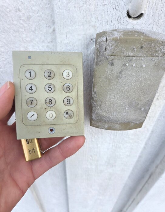 Gammal, smutsig kodpanel med tangenter och en löst batteri visas mot en vit vägg, alternativ till trasig garagedosa.