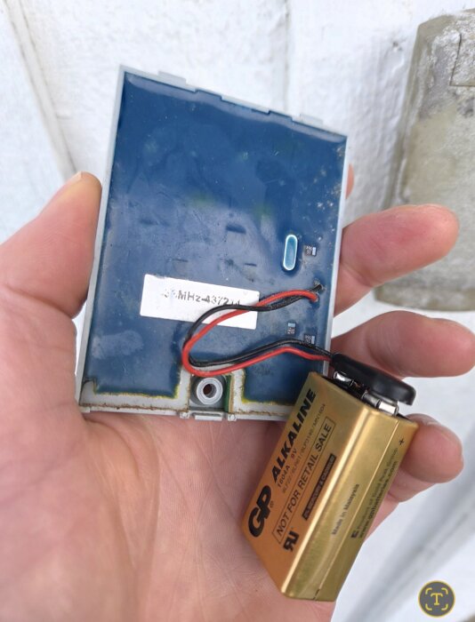 Hand håller trasig garageportkontroll med batteri exponerat.