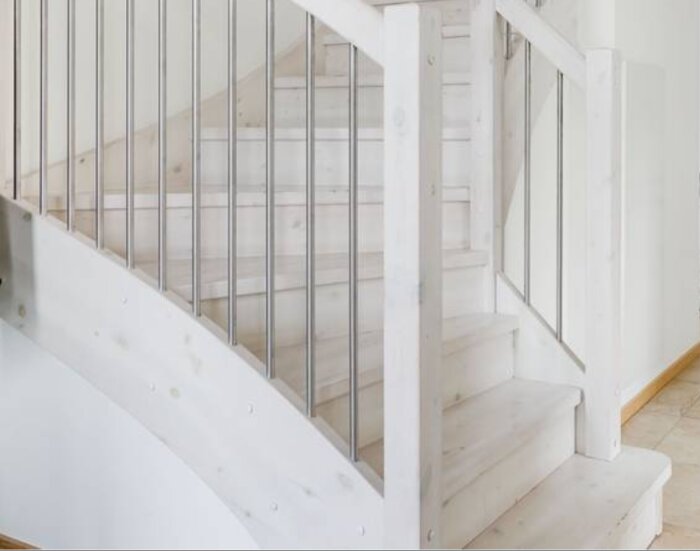 Vitmålad trappa med rektangulära steg och vertikala metallspjälor, fokus på första steget som behöver avslutas snyggt i renoveringsprojekt.