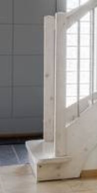 Trappsteg i trä vid foten av en vitmålad trappa, fokus på det första steget och räckets nederdel.