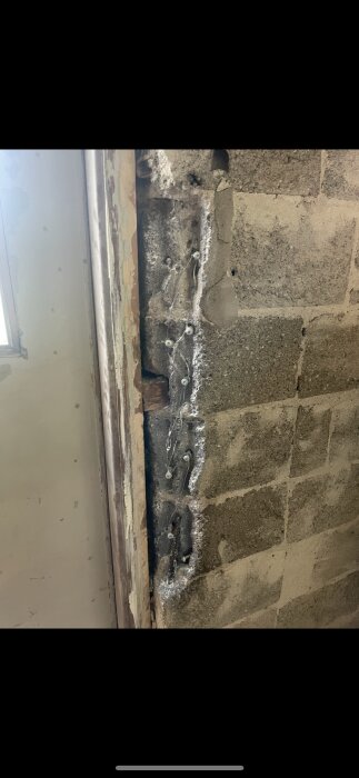 Reparerad spricka i hålstensvägg nära ett fönster, med armeringsjärn och murbruk synligt.