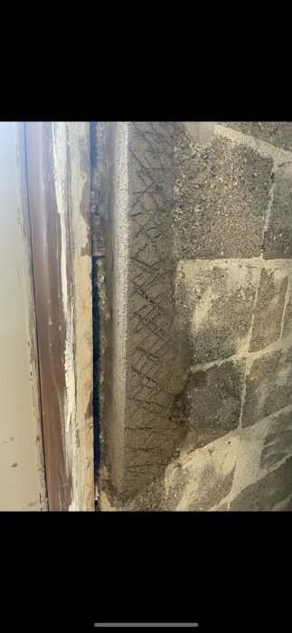 Närbild på en lagad spricka i en hålstensvägg, delvis täckt med reparationsbetong, intill en dörrkarm.