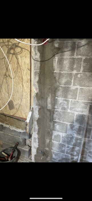 Renoverad vägg med putsade ytor och elektriska ledningar, osb-skiva synlig, verktyg i hink bredvid väggen.