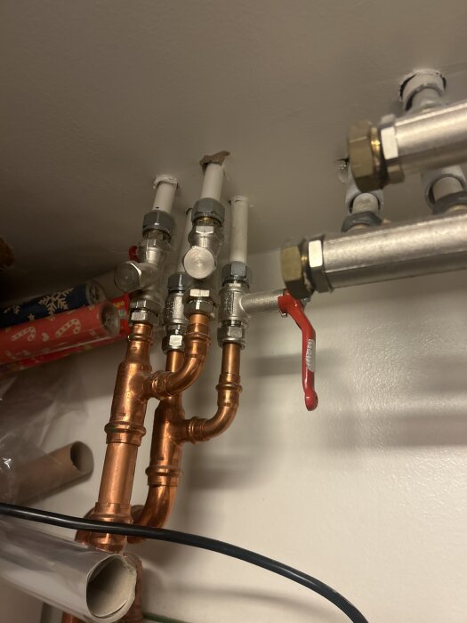 Smutsfilter på returledning med avstängning på tillopp visas med koppar- och vita rör, omgivna av inställningar i fjärrvärmesystem.